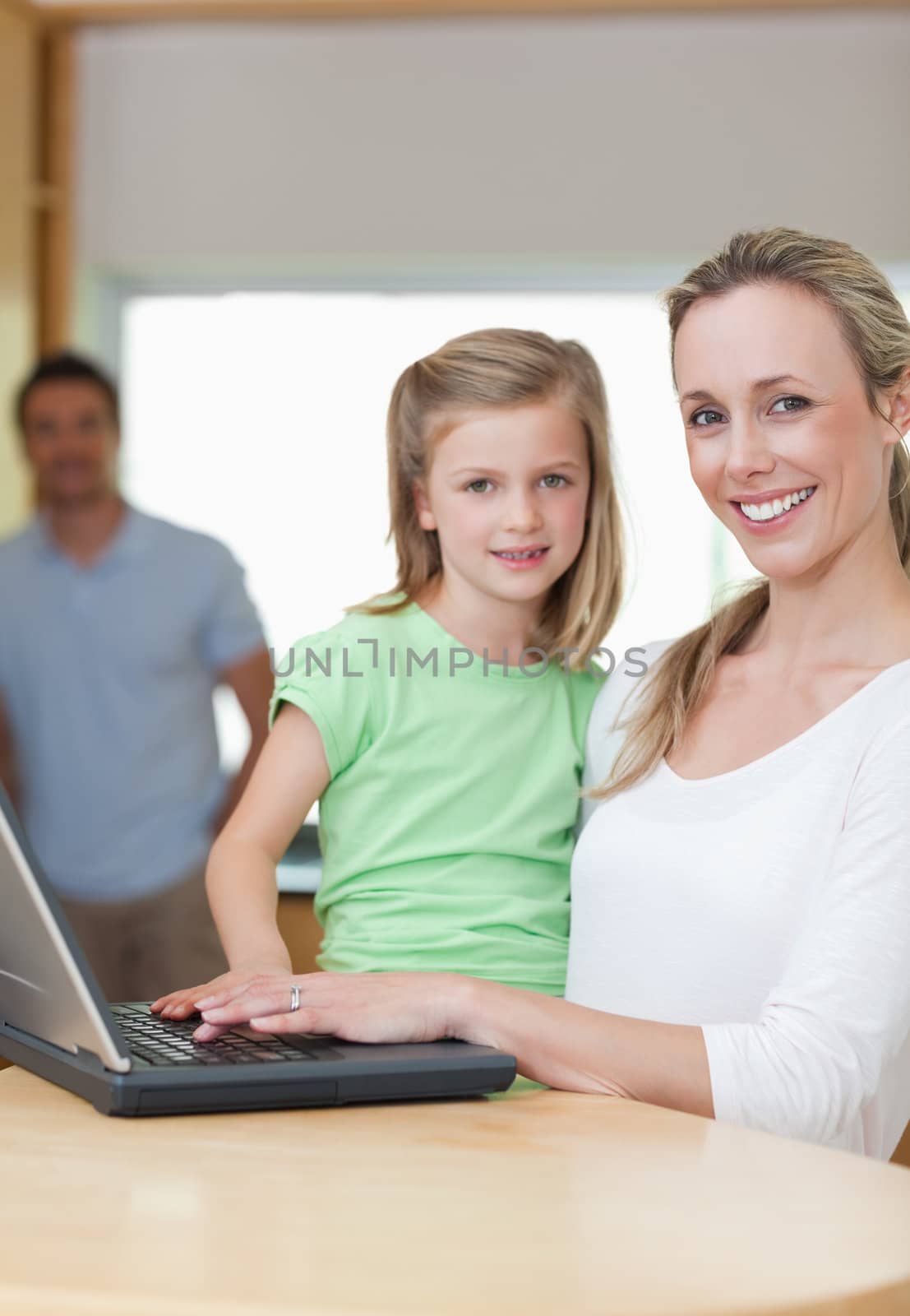 Mother and daughter using notebook together with father in the background