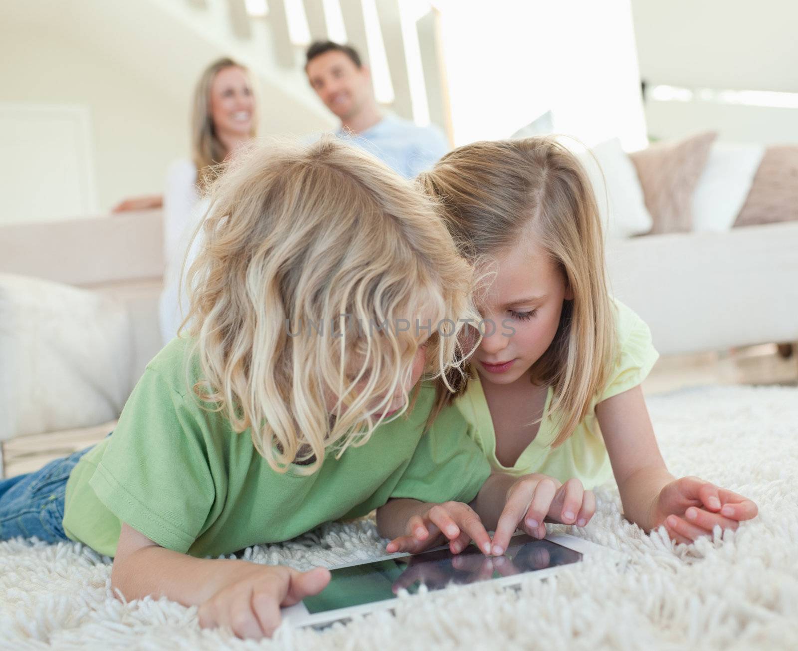 Siblings on the floor together with tablet and parents behind them