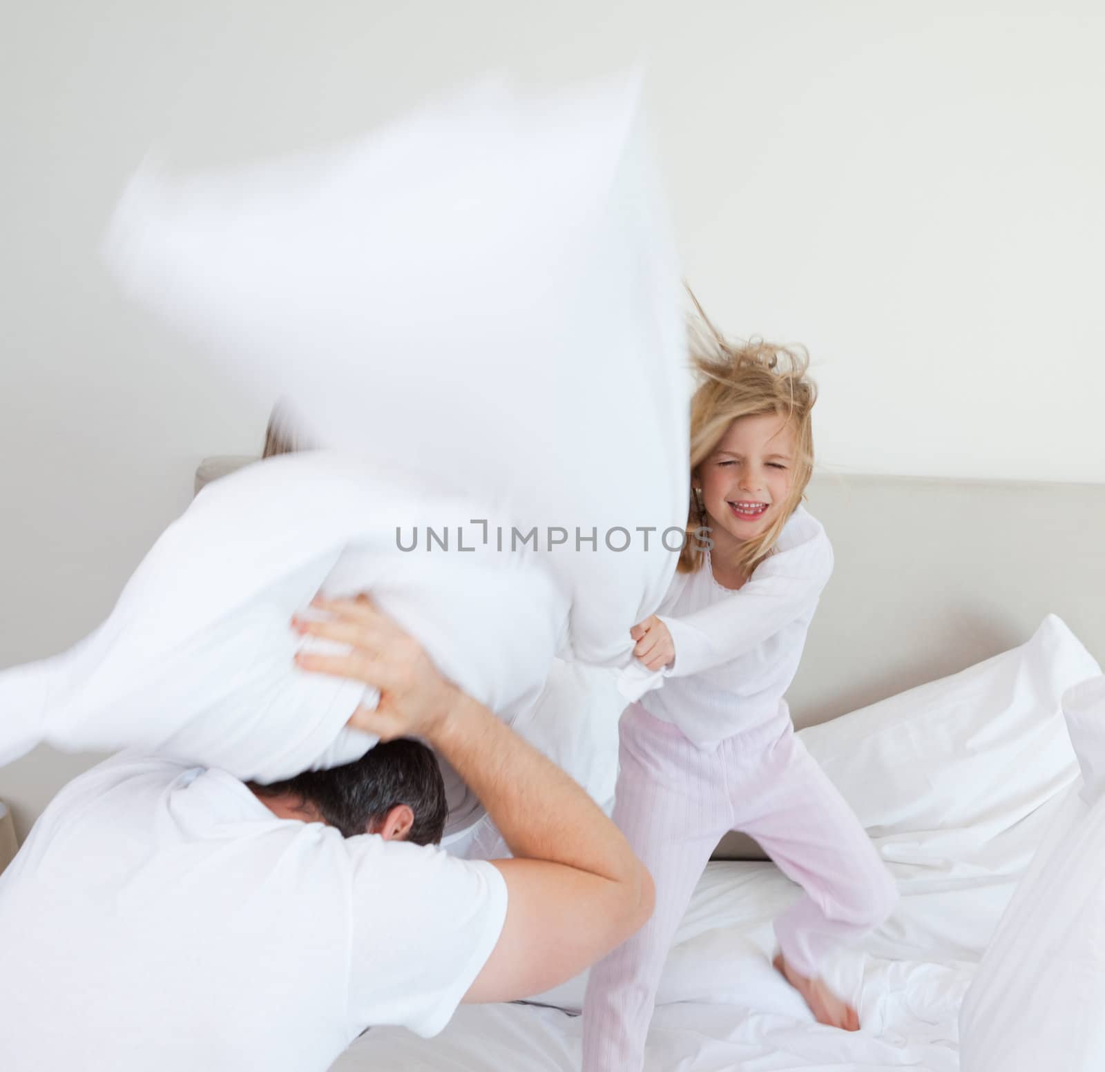 Little girl hitting her father with pillow