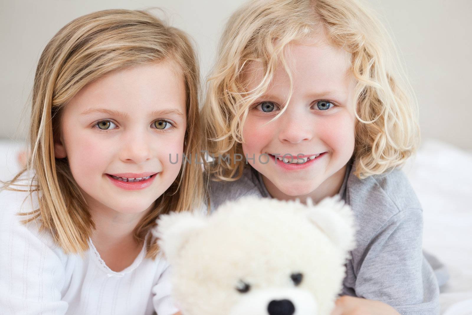 Siblings lying on the bed together with their teddy