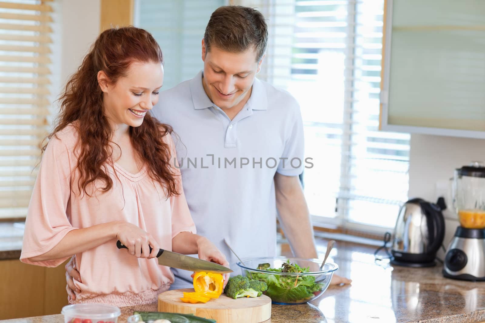Man watching his girlfriend preparing a salad in the kitchen