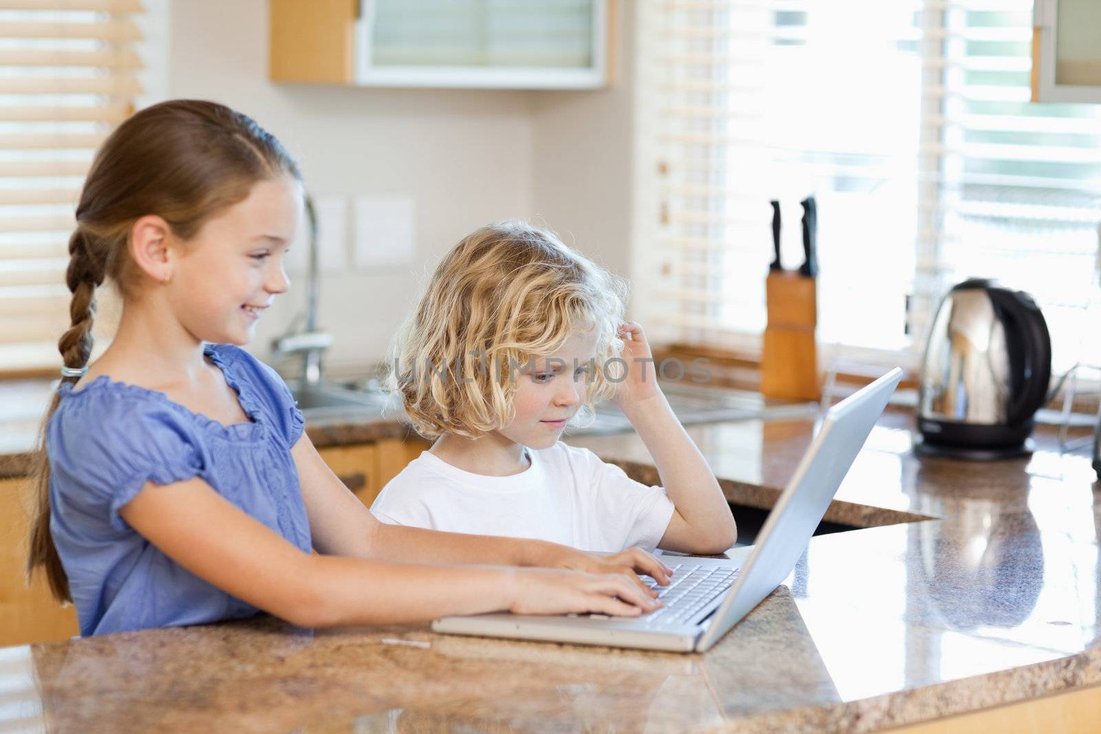 Siblings together on the laptop in the kitchen