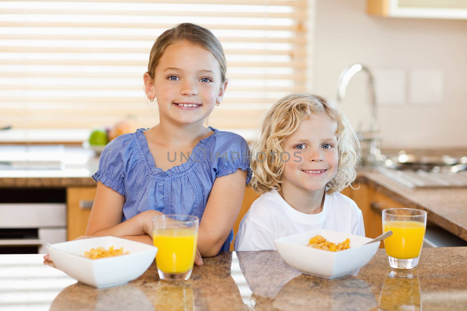Smiling siblings with breakfast behind the kitchen counter
