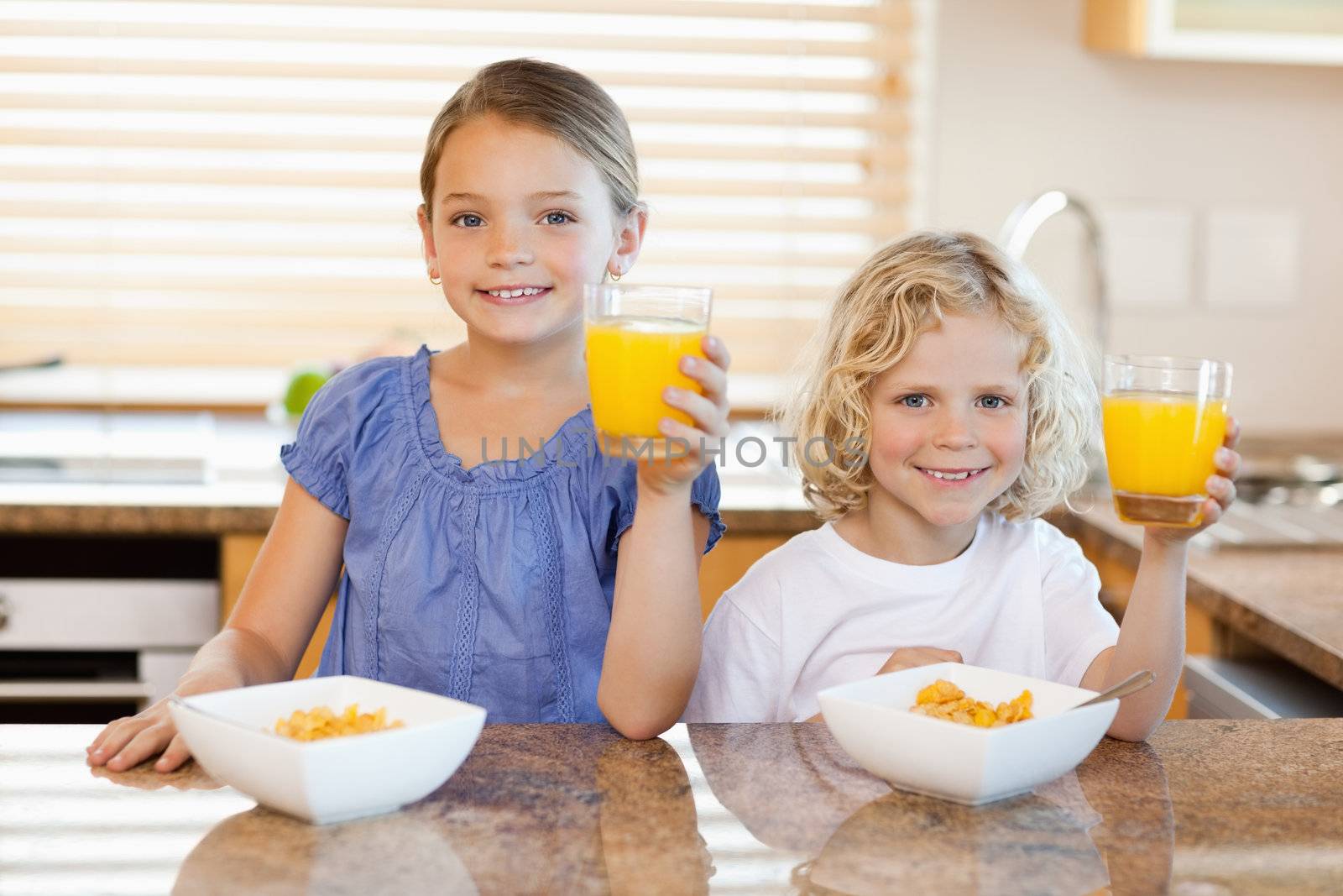 Siblings in the kitchen rising their glasses of orange juice