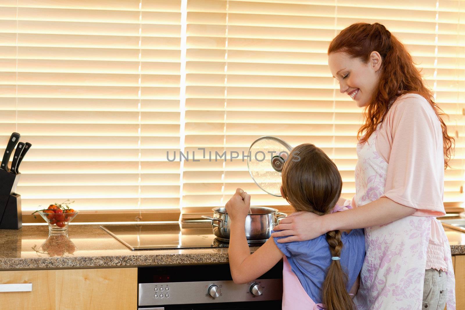 Cheerful smiling mother showing her daughter how to cook