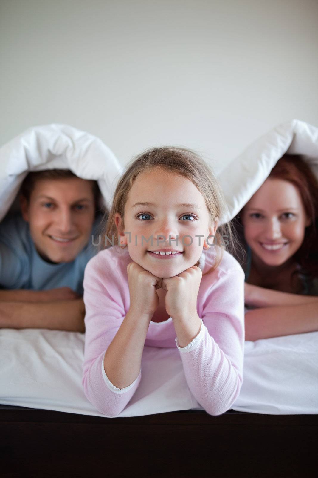 Smiling girl under bed cover with her parents by Wavebreakmedia