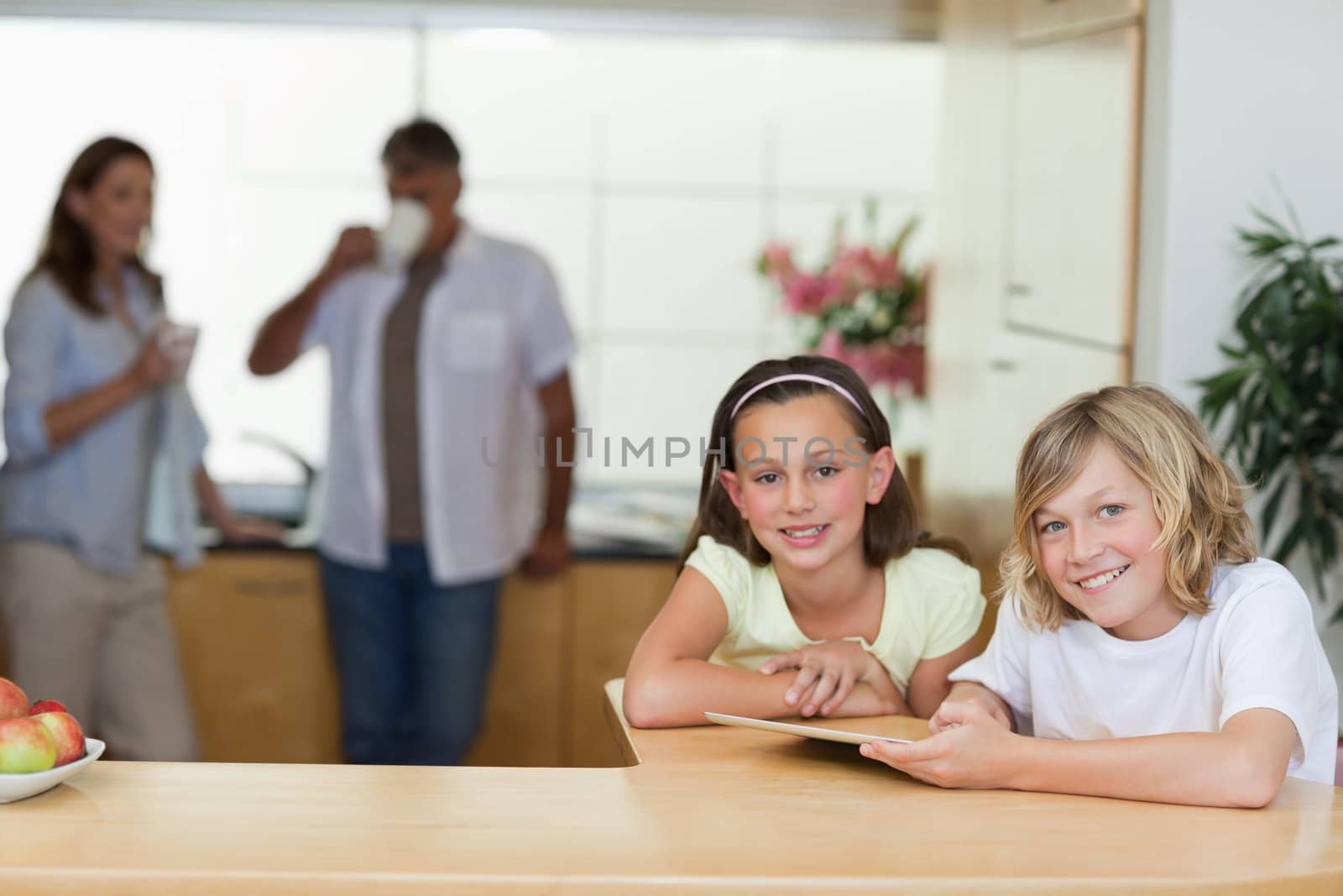 Siblings using tablet in the kitchen with their parents behind them