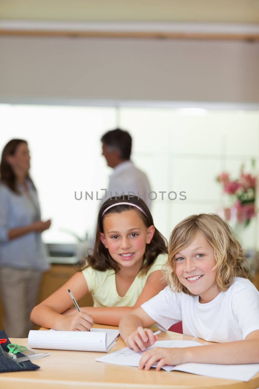 Children doing homework with their parents behind them by Wavebreakmedia