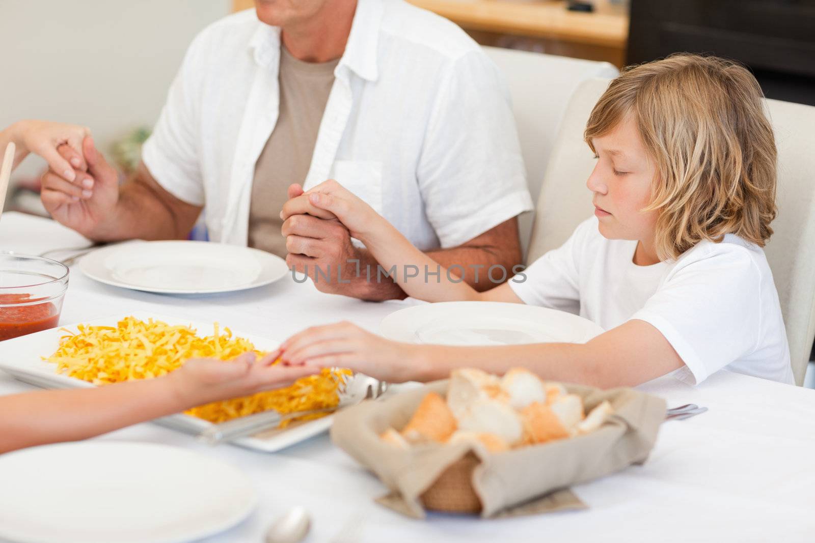 Family saying a prayer before dinner by Wavebreakmedia