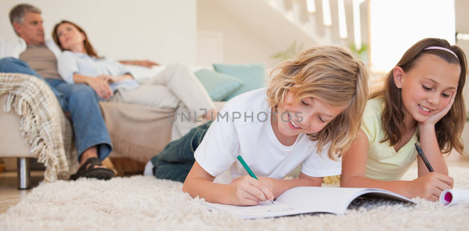 Siblings doing their homework on the carpet with their parents behind them