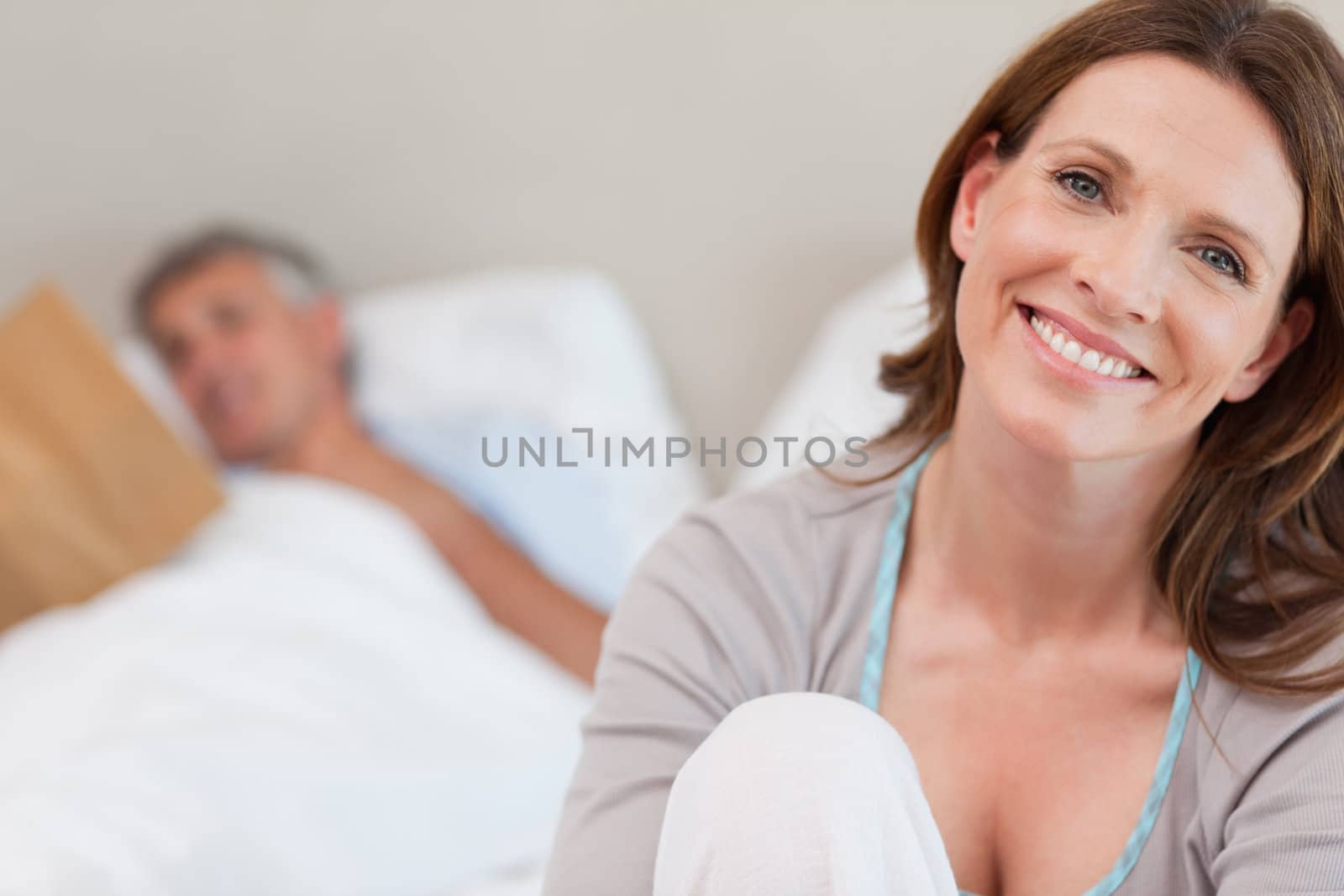 Smiling mature woman on the bed with reading husband behind her
