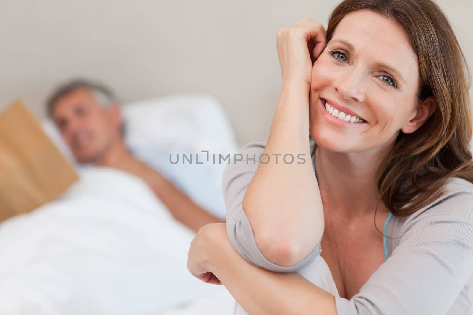 Happy smiling woman on the bed with husband reading behind her