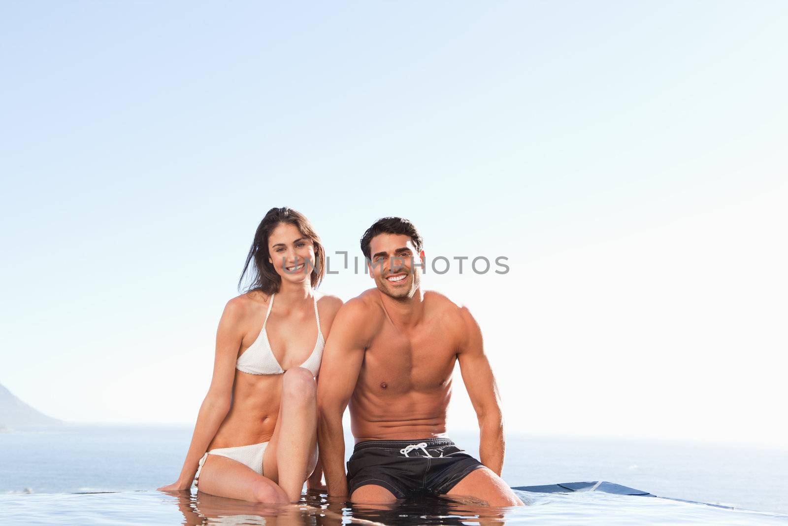 Smiling couple sitting on the pool edge
