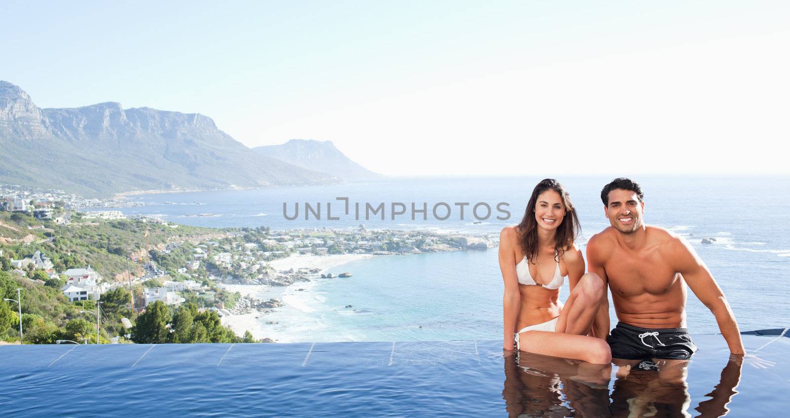 Couple sitting on the pool edge with landscape in the background