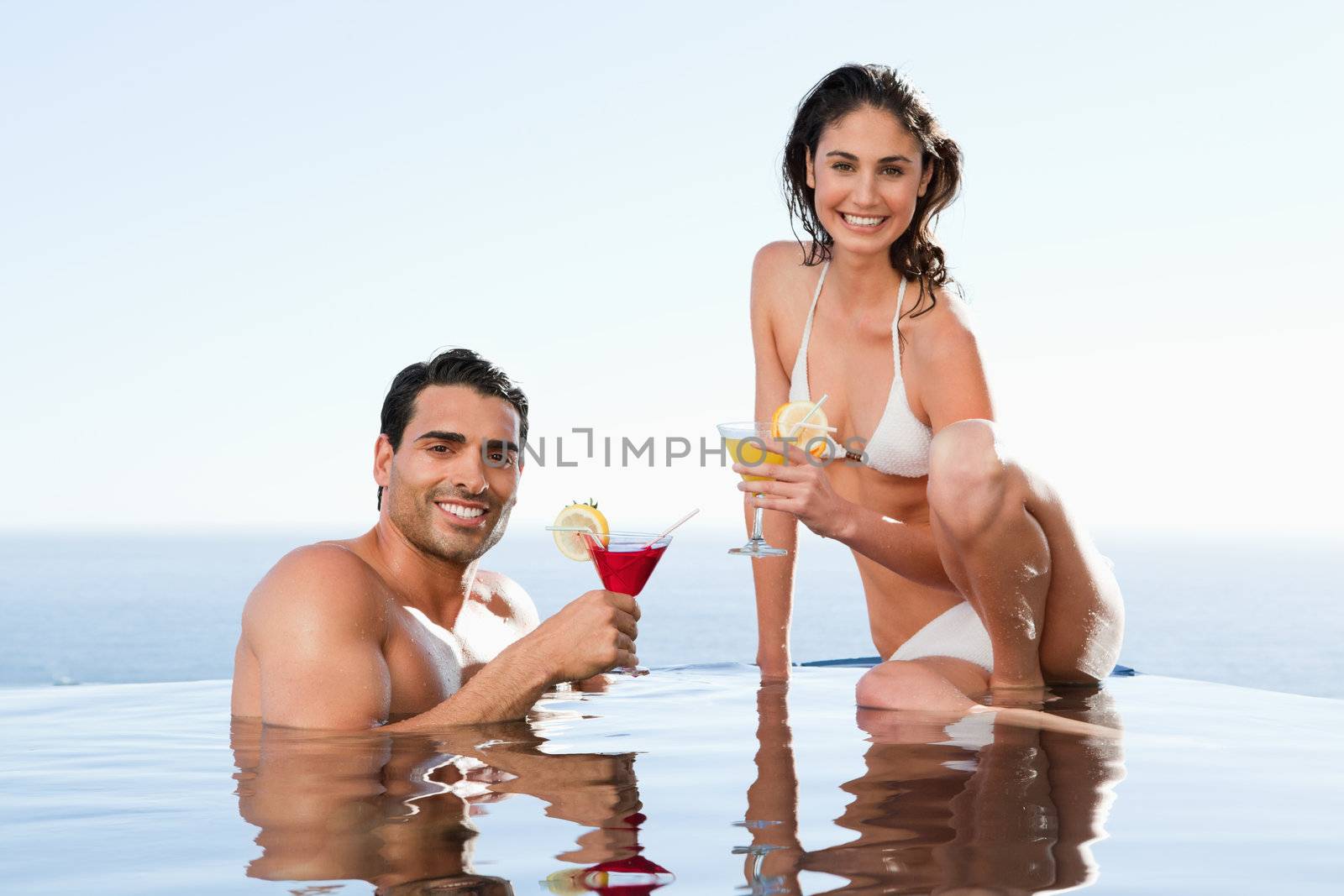 Cheerful young couple having cocktails in the pool