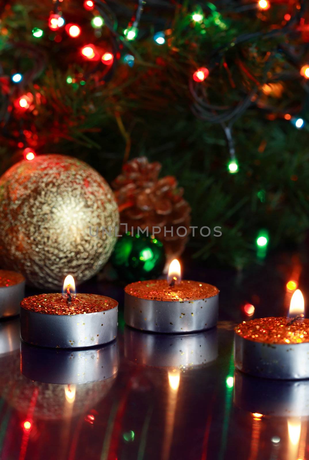 Few lighting candles on glass surfase with reflection on background with Christmas decorations