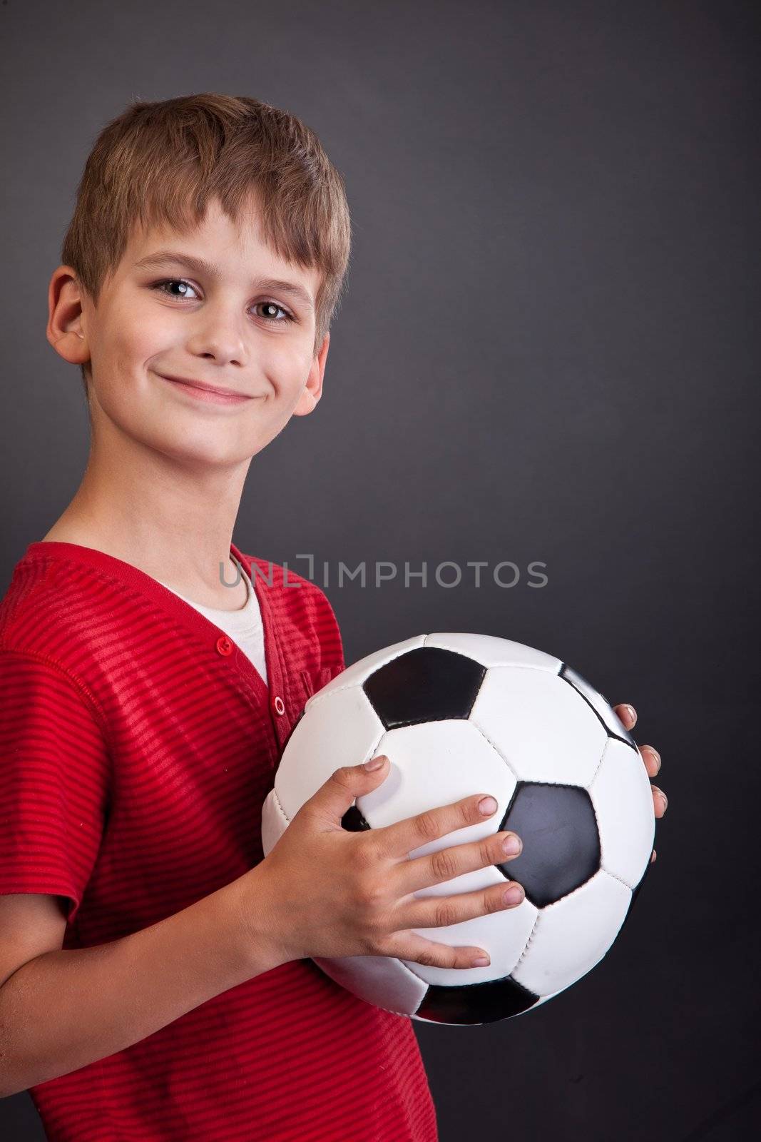 Cute boy is holding a football ball made of genuine leather isolated on a black background. Soccer ball