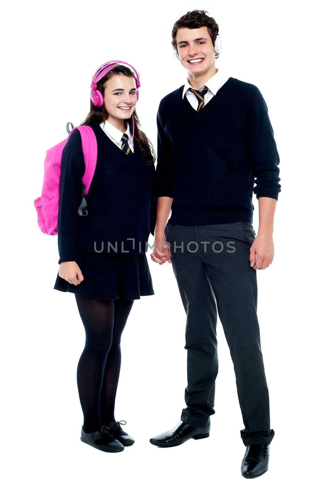 School friends with headphones on enjoying music. Holding hands, full length portrait