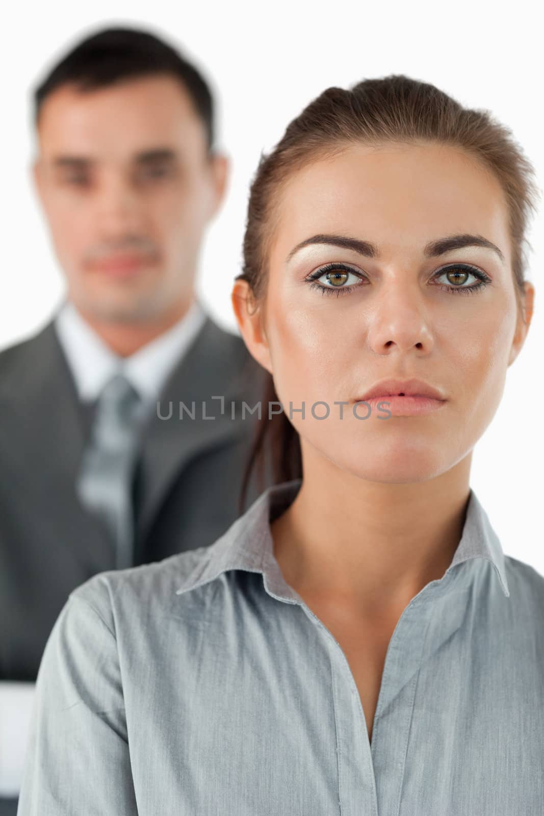 Close up of serious looking businesswoman with colleague behind her against a white background
