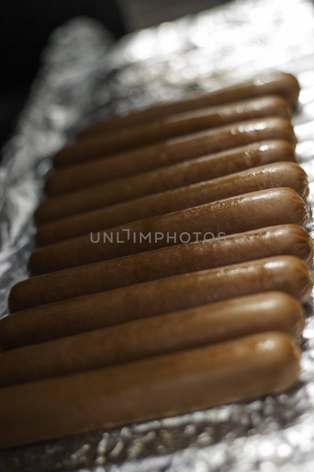 Row of tasty brown sausages being grilled on tinfoil with shallow dof