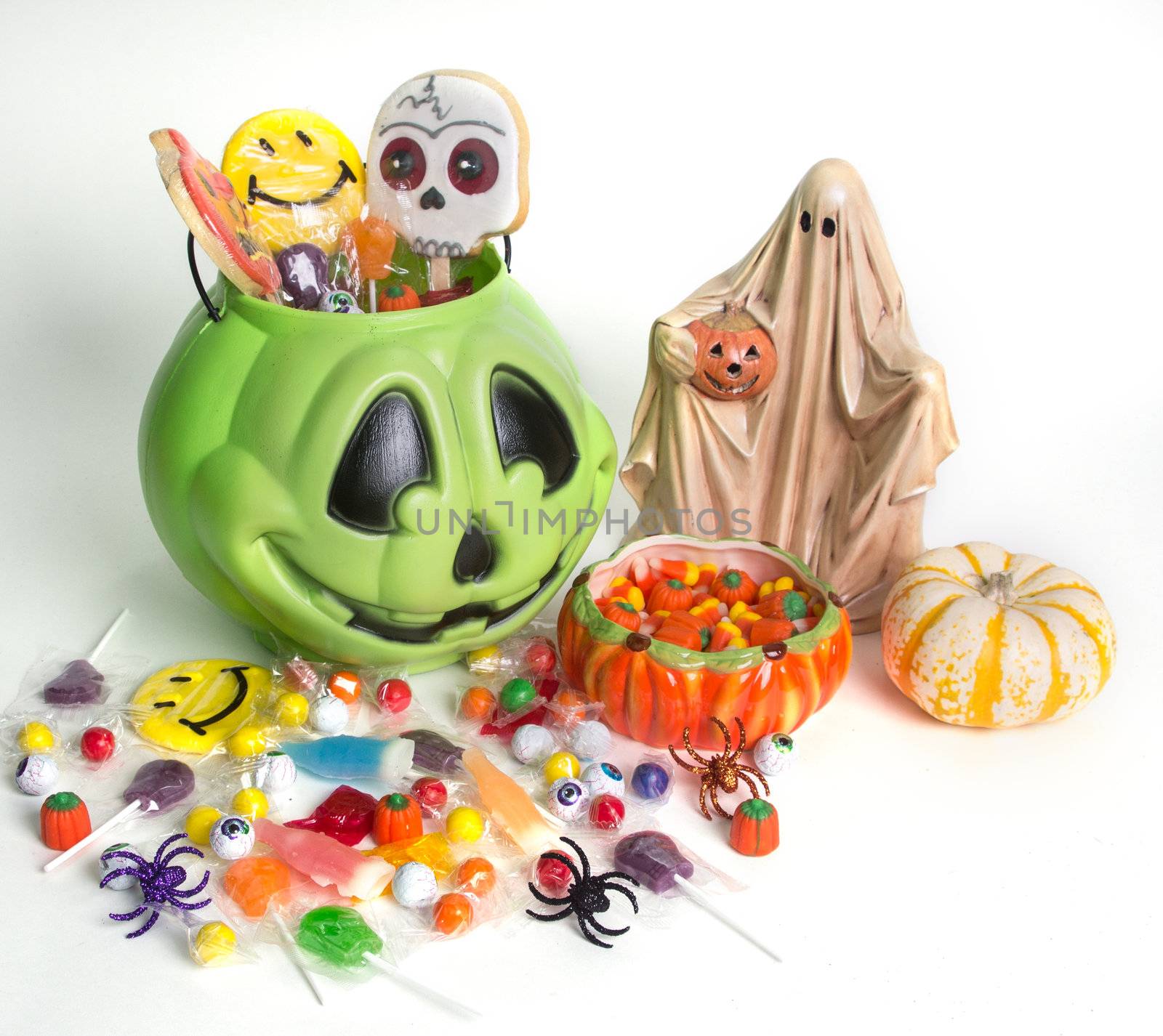 Green pumpkin halloween bucket filled with candy, candy corn, suckers, and cookies.  Isolated on white background