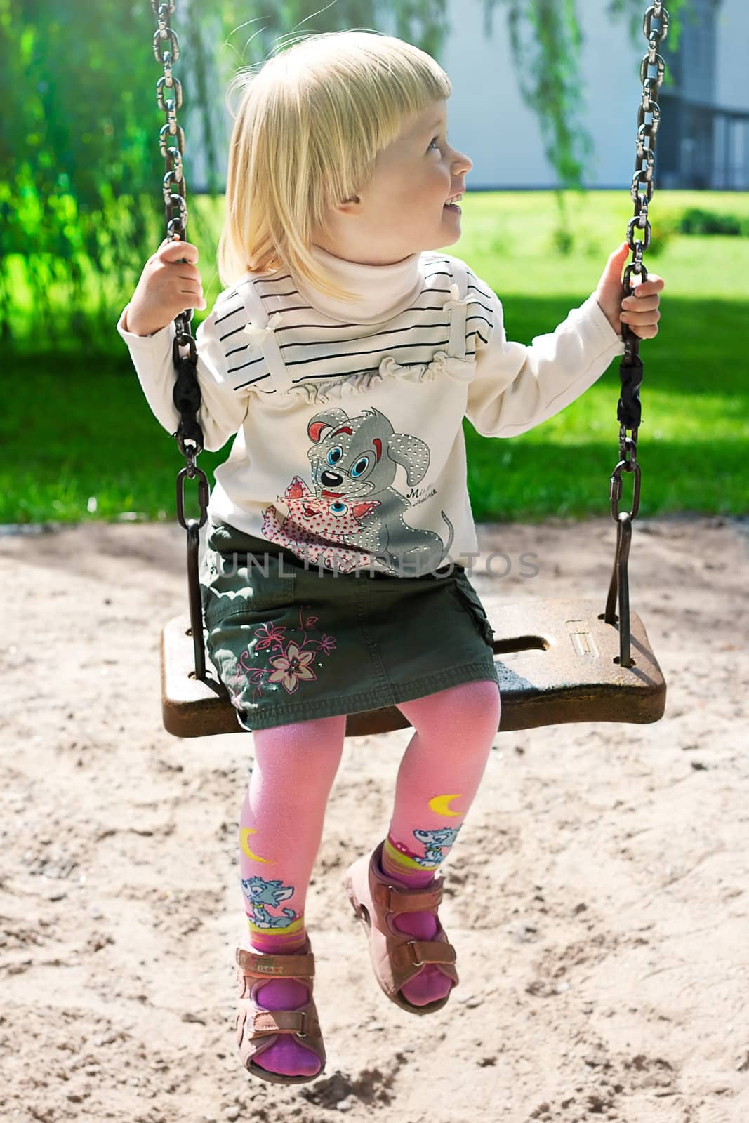 Happy little girl riding on a swing in the park shooting