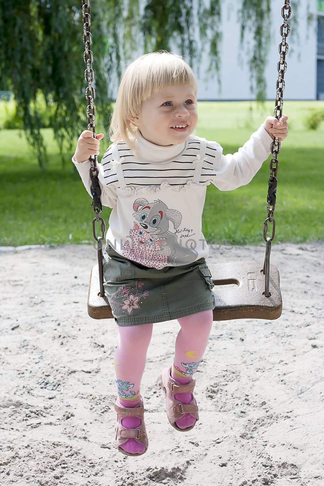 Happy little girl riding on a swing in the park shooting