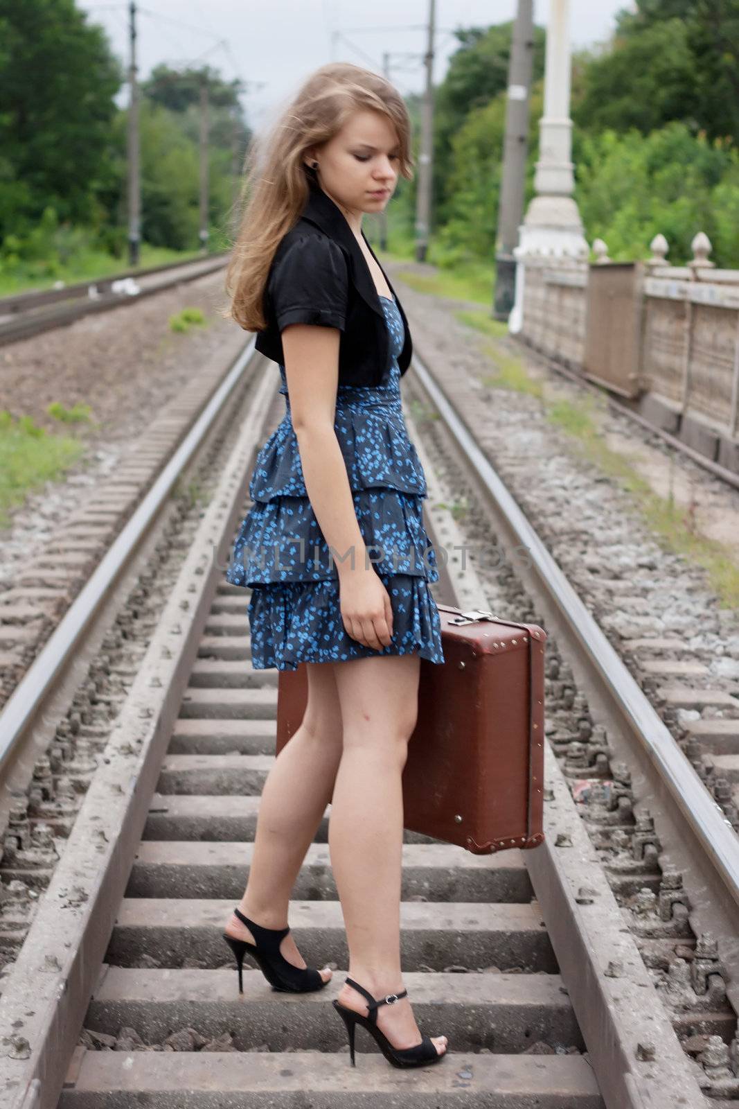 Girl with a suitcase standing on the rails shooting outdoors