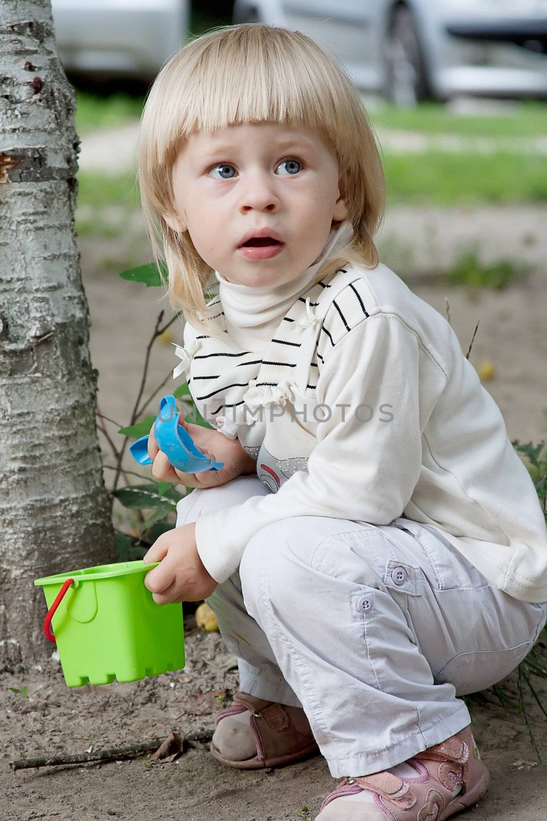 Happy little girl sitting in the sandbox at the park shooting