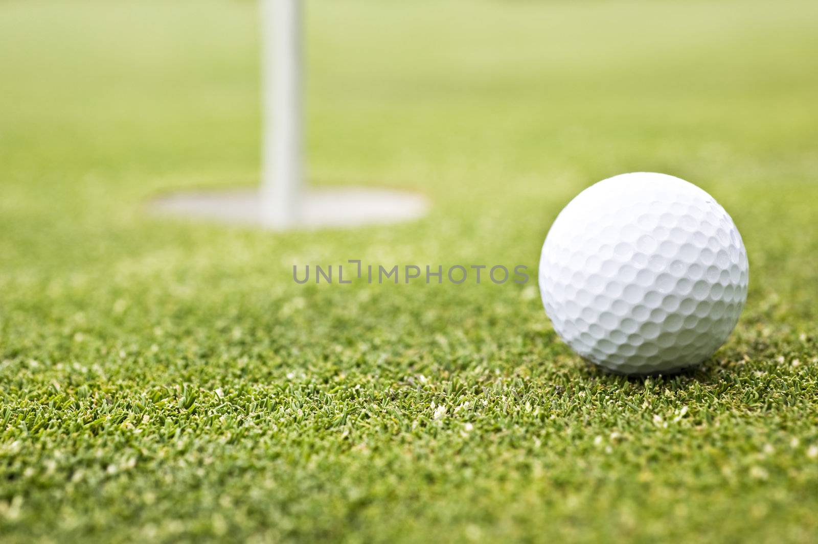 Golf ball on a putting green with the flag in the background - very shallow depth of field