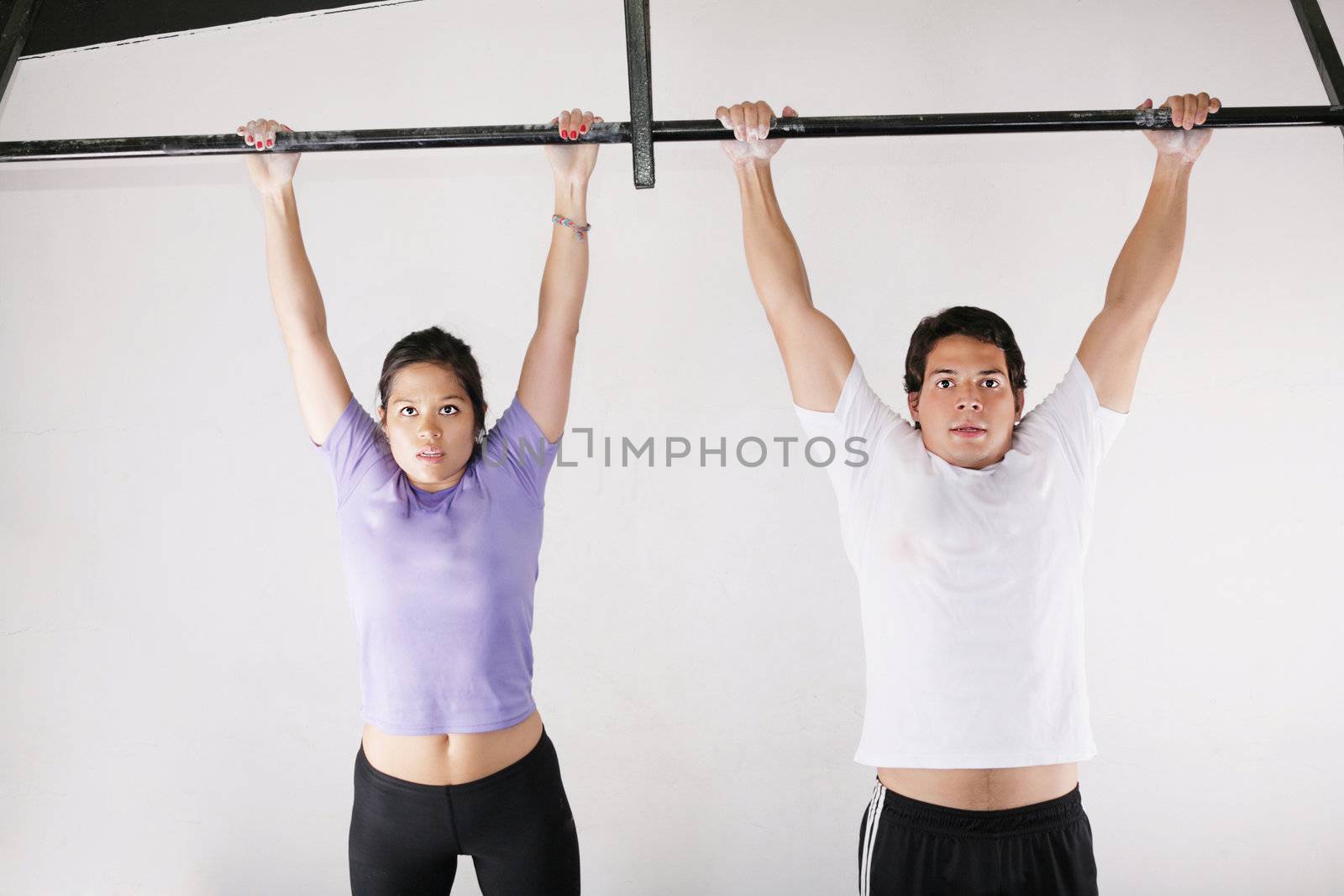 Female and male bodybuilder doing pull-ups on metal bar on gym