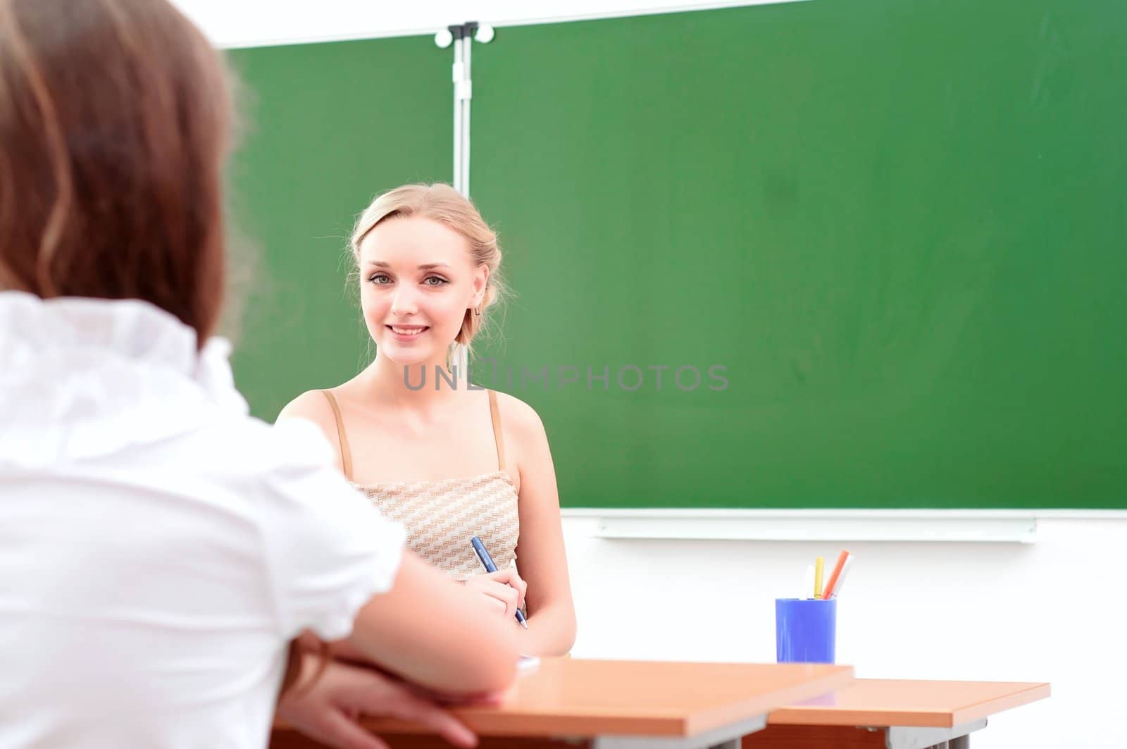 portrait of beautiful young teacher, sits at a desk in the classroom