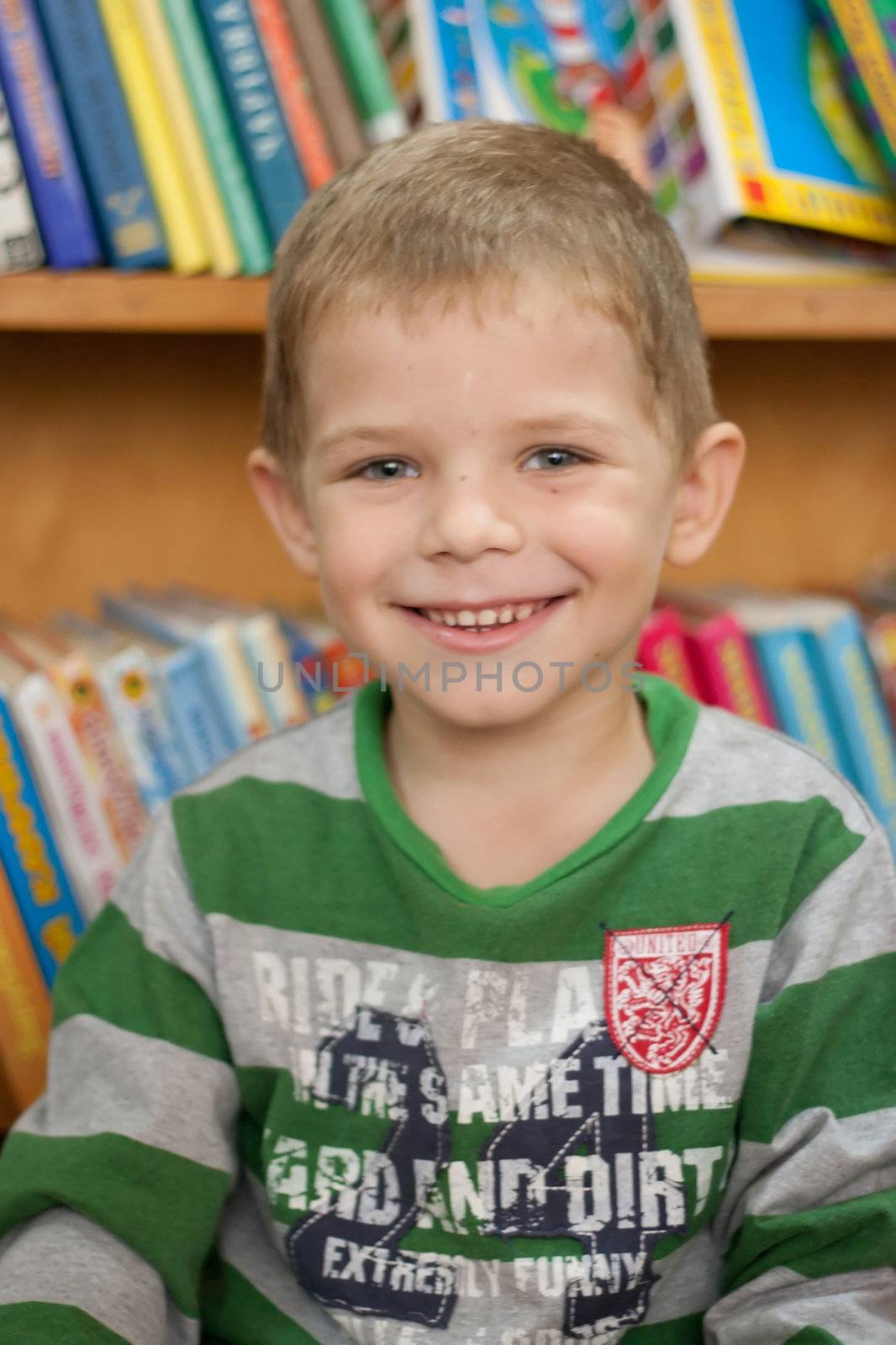 small boy smiling on the background of the books in the library