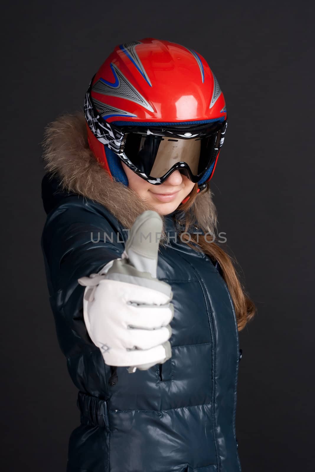 A girl in a ski helmet and goggles raises a big thumbs up