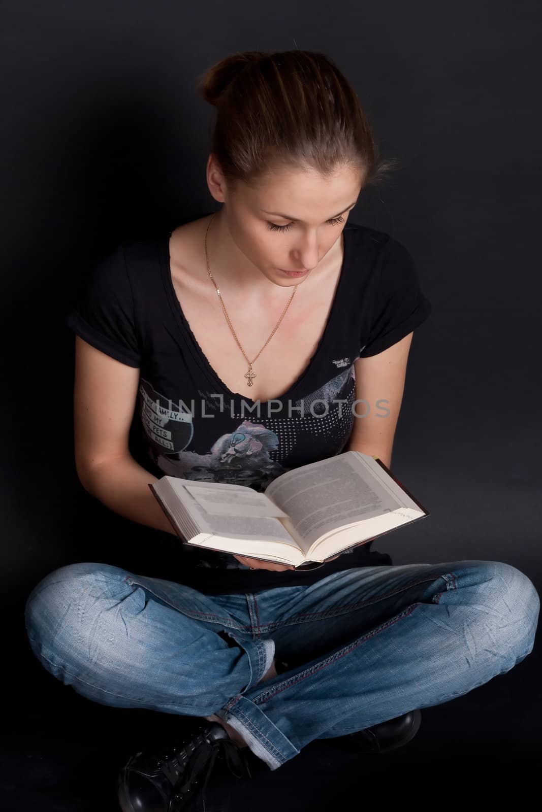 The girl in blue jeans sitting on the floor and reading a book studio photography