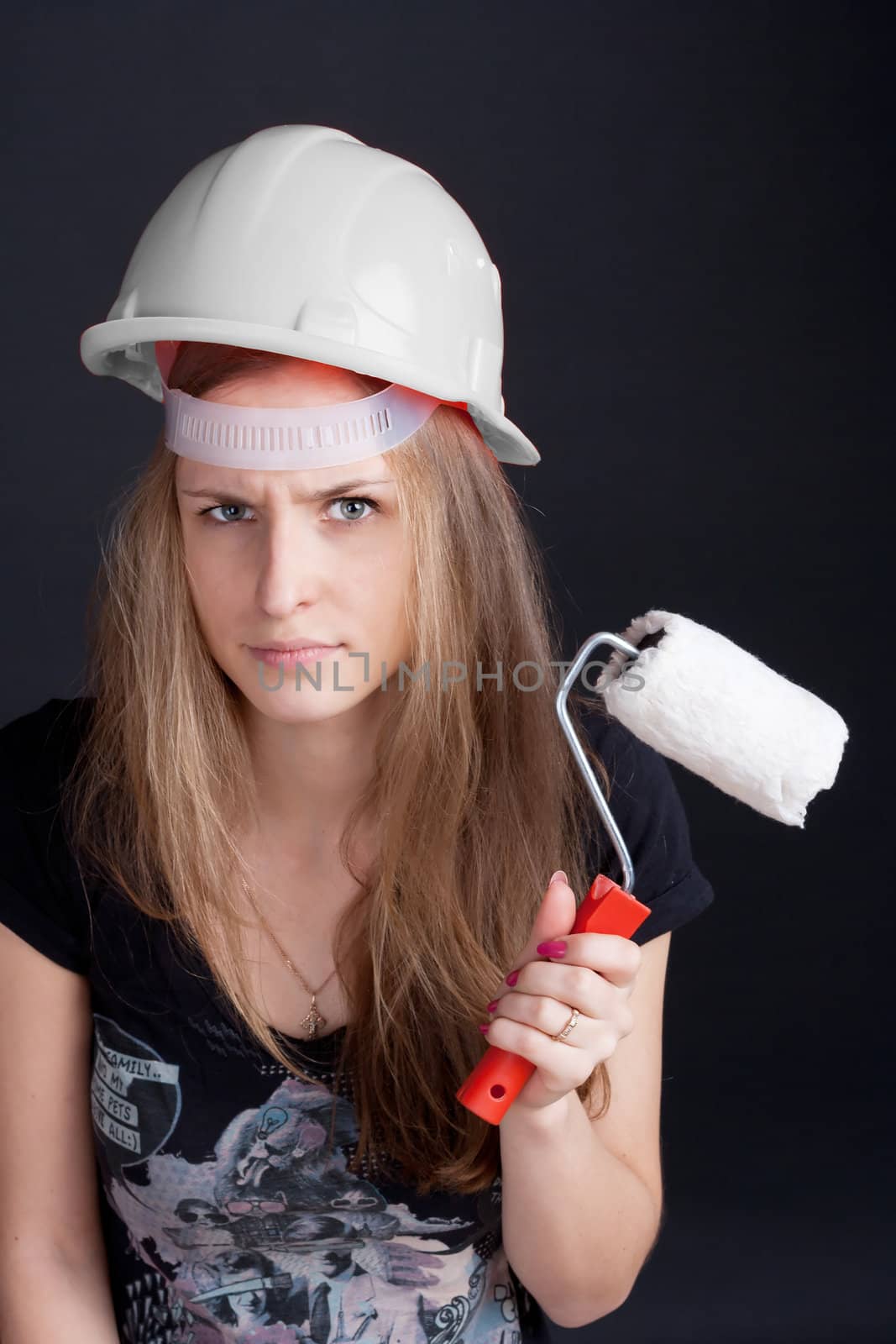 The girl in the construction helmet with a roller in his hand against a dark background