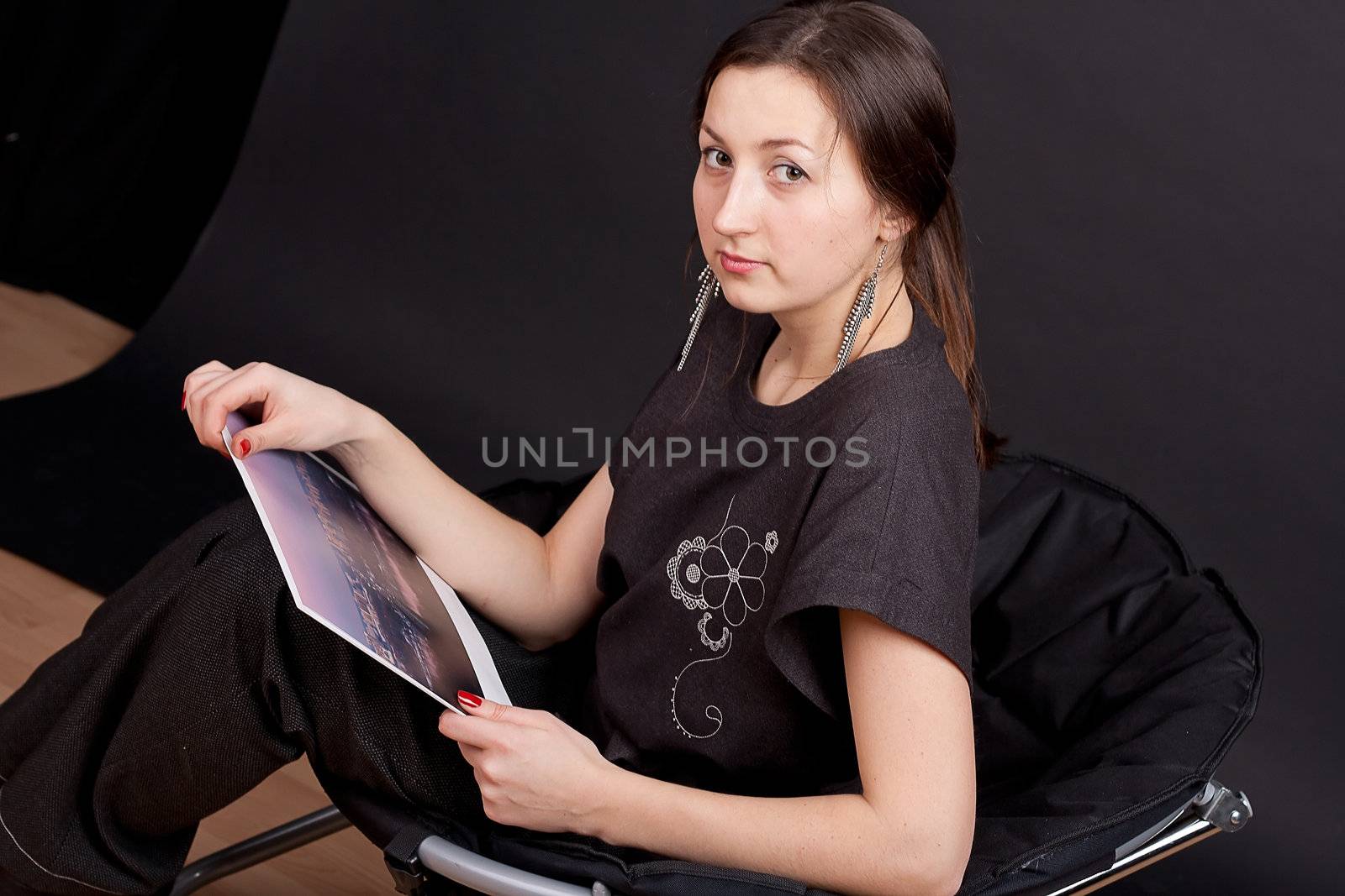 A serious girl sitting on a chair and looks into the camera studio photography