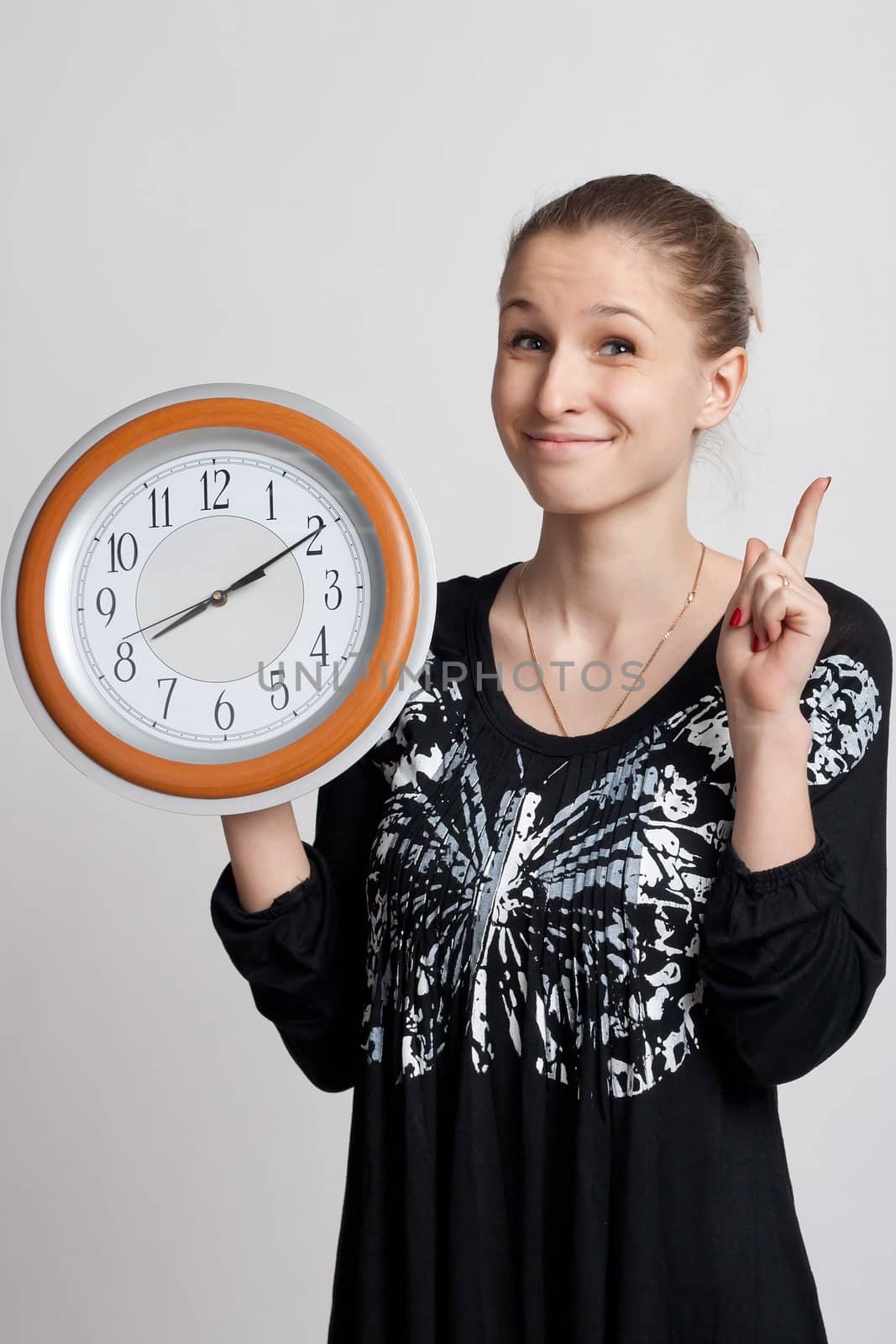 beautiful girl with a big clock in his hand raises his index finger up