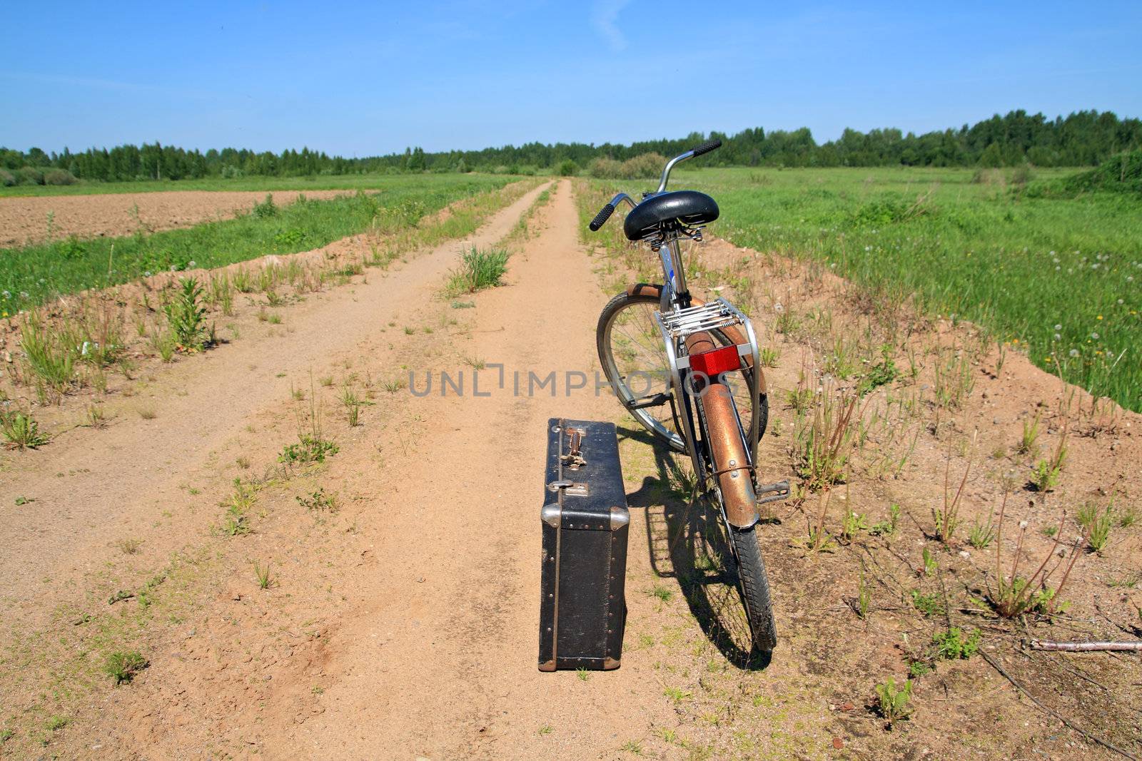 old valise near old bicycle on rural road