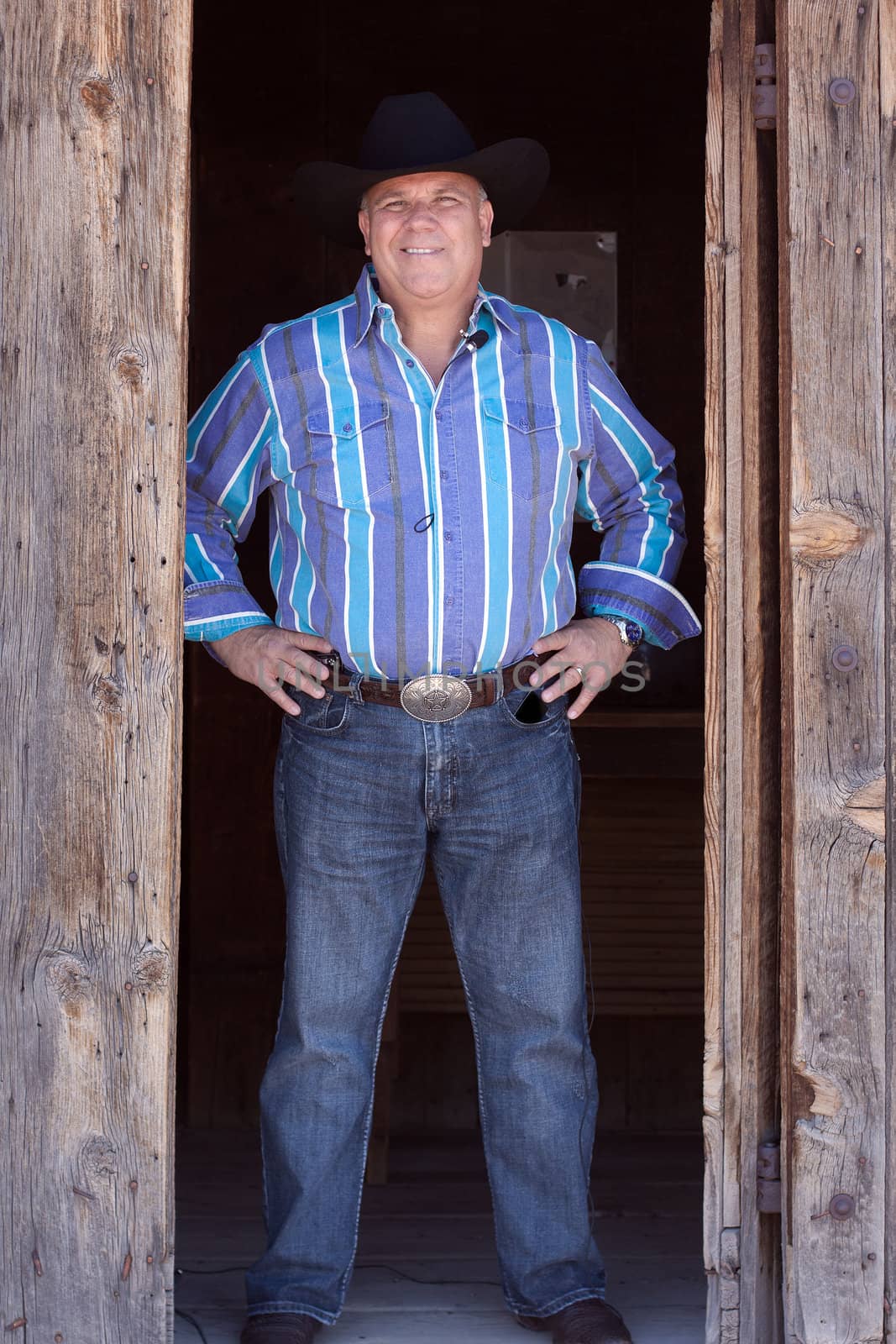 Texas cowboy standing in doorway of barn in jeans and western shirt