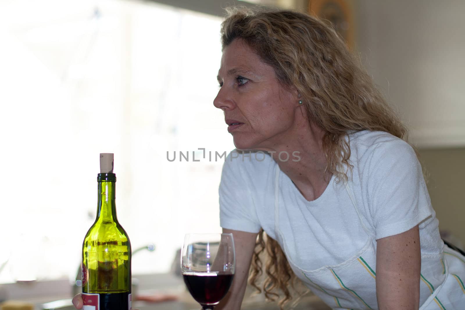 Depressed woman, drinking wine in kitchen during the day