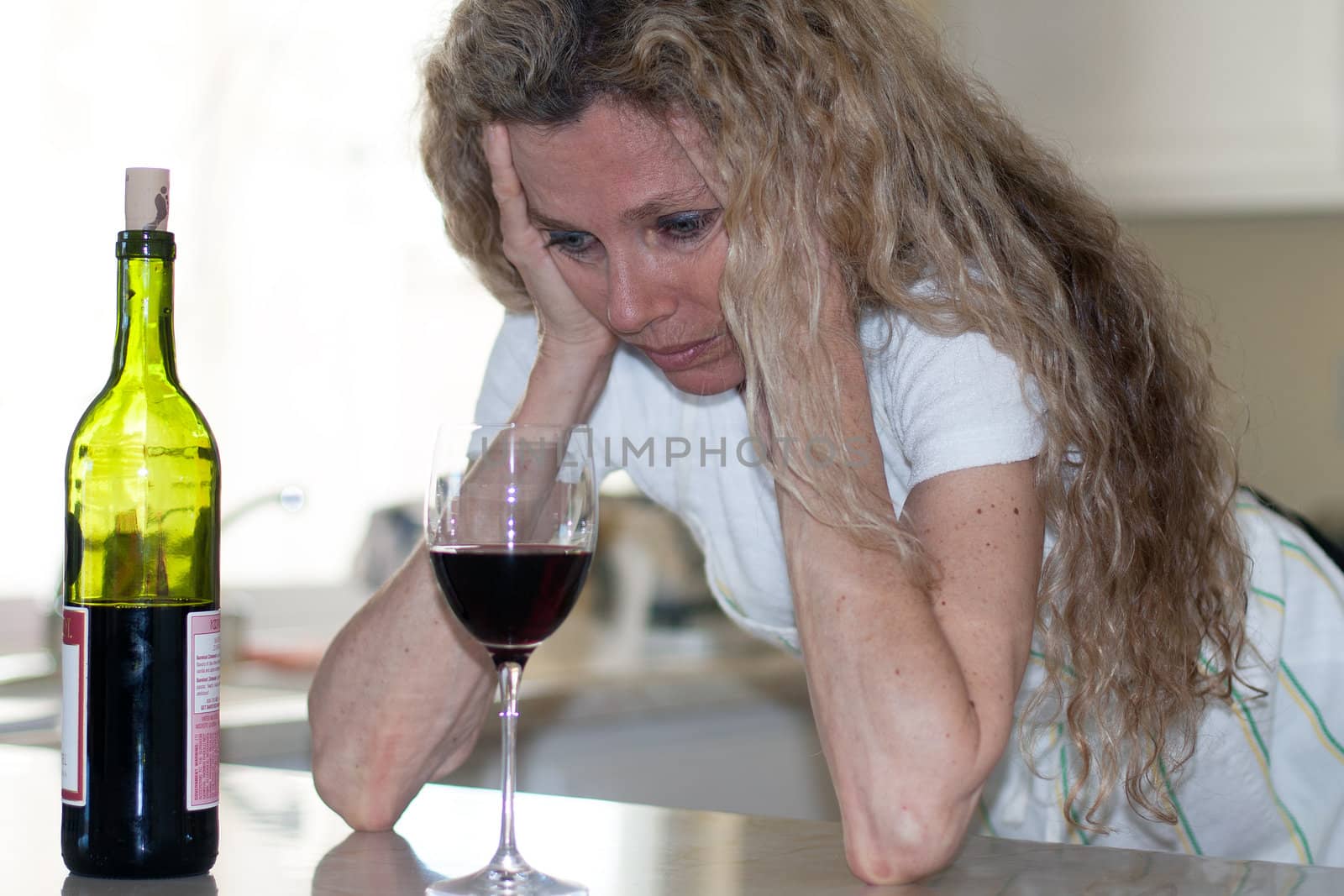 Depressed woman, drinking wine in kitchen during the day