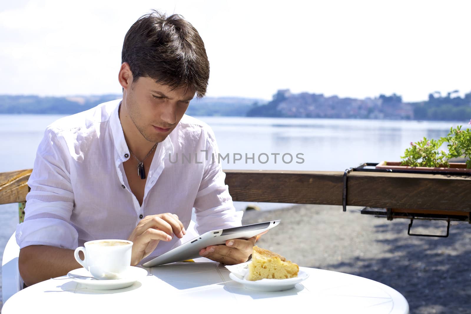 Young man in italy reading tablet during breakfast in front of beautiful lakez