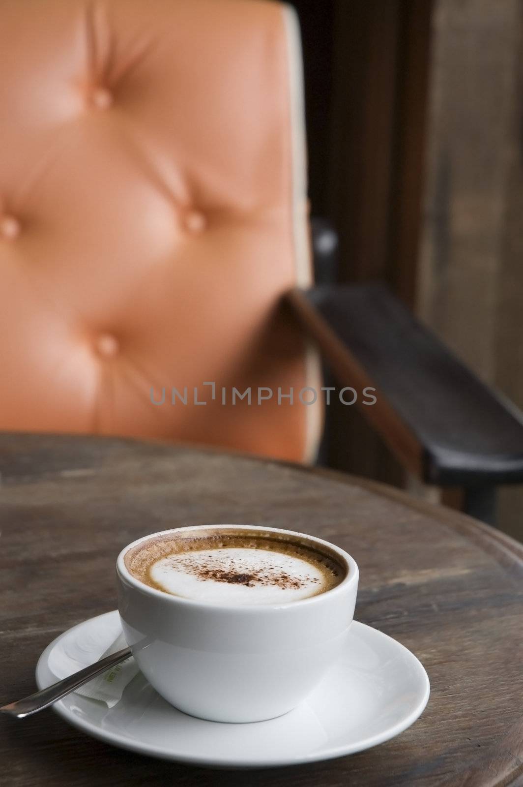 A cup of Cappuccino on wooden table with orange armchair background
