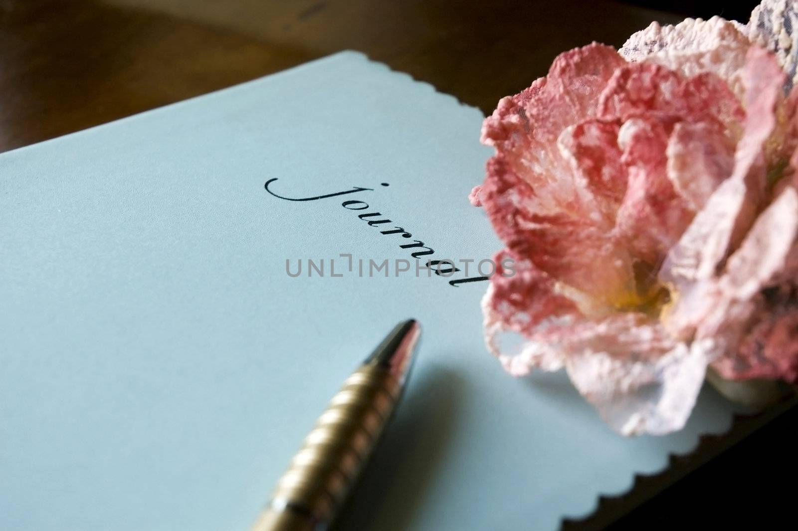 Blue journal book put on table with pen and pink flower. 