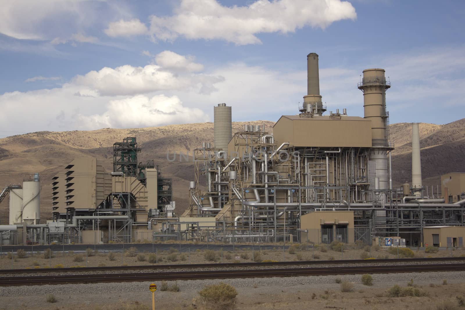 Power plant factory next to train track in the desert with blue cloudy skies