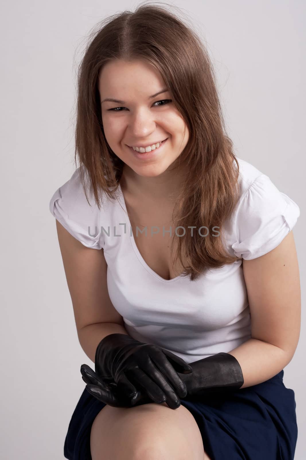 A girl sits in a light shirt and black gloves on a light background