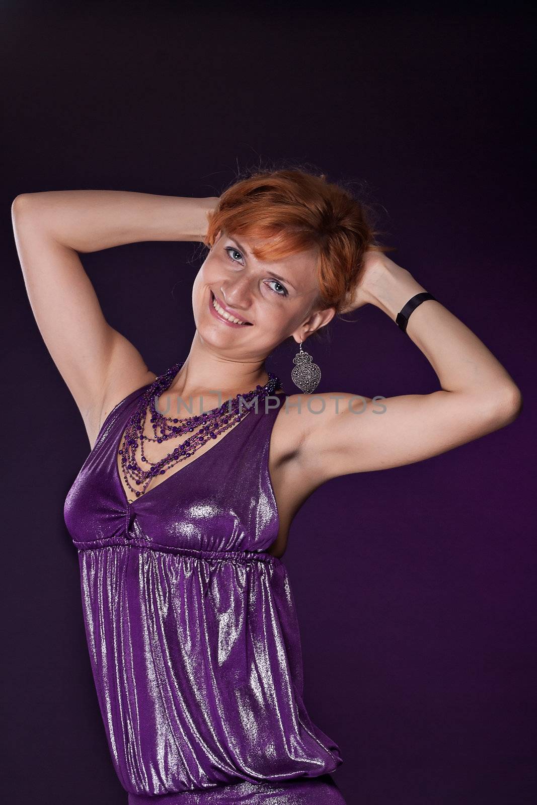  Red-haired girl in a purple dress on a dark background. Studio photography