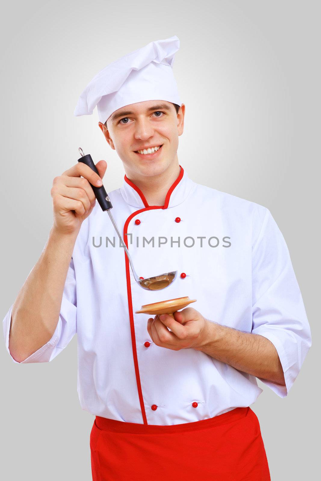 Young male chef in red apron against grey background