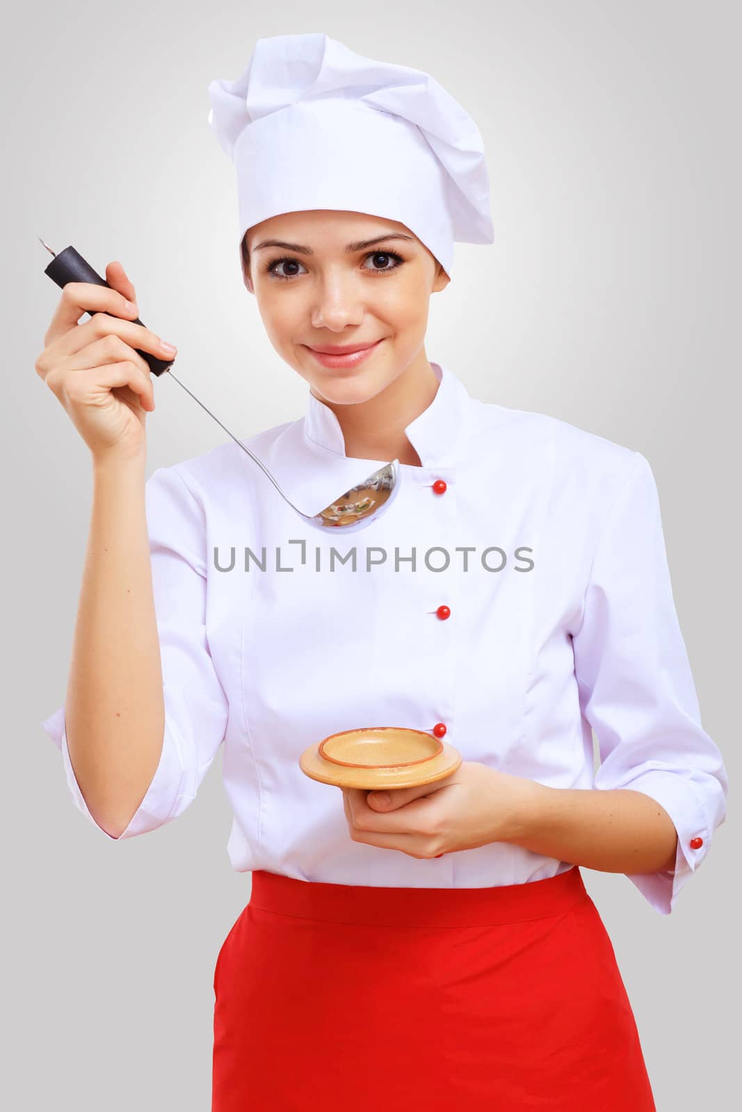 Young female chef in red apron against grey background